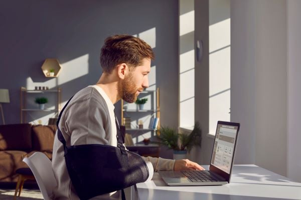 Man with cast on arm working from home in front of laptop