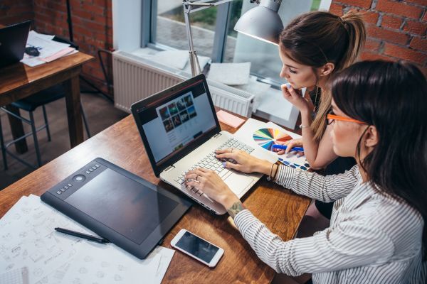 Two women sitting at a laptop designing website